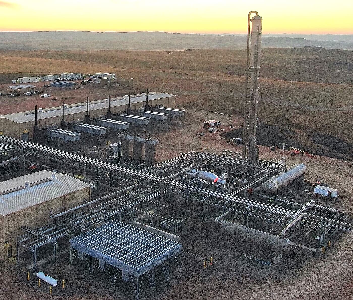 Aerial view of a natural gas processing plant at dusk, with treating towers, compressor buildings and pipe racks on open plains